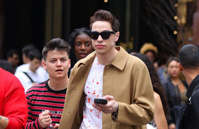 24d4d2d9e73e4fa3e62cd33a45b41e63 Pete Davidson walking through a crowd in New York City wearing sunglasses and a tan coat, holding his phone, July 2025