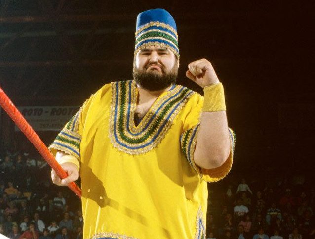 akeem-3-e1665739791734 Akeem 'The African Dream' WWE wrestler in yellow African-inspired costume with traditional hat and staff during controversial 1980s character transformation"